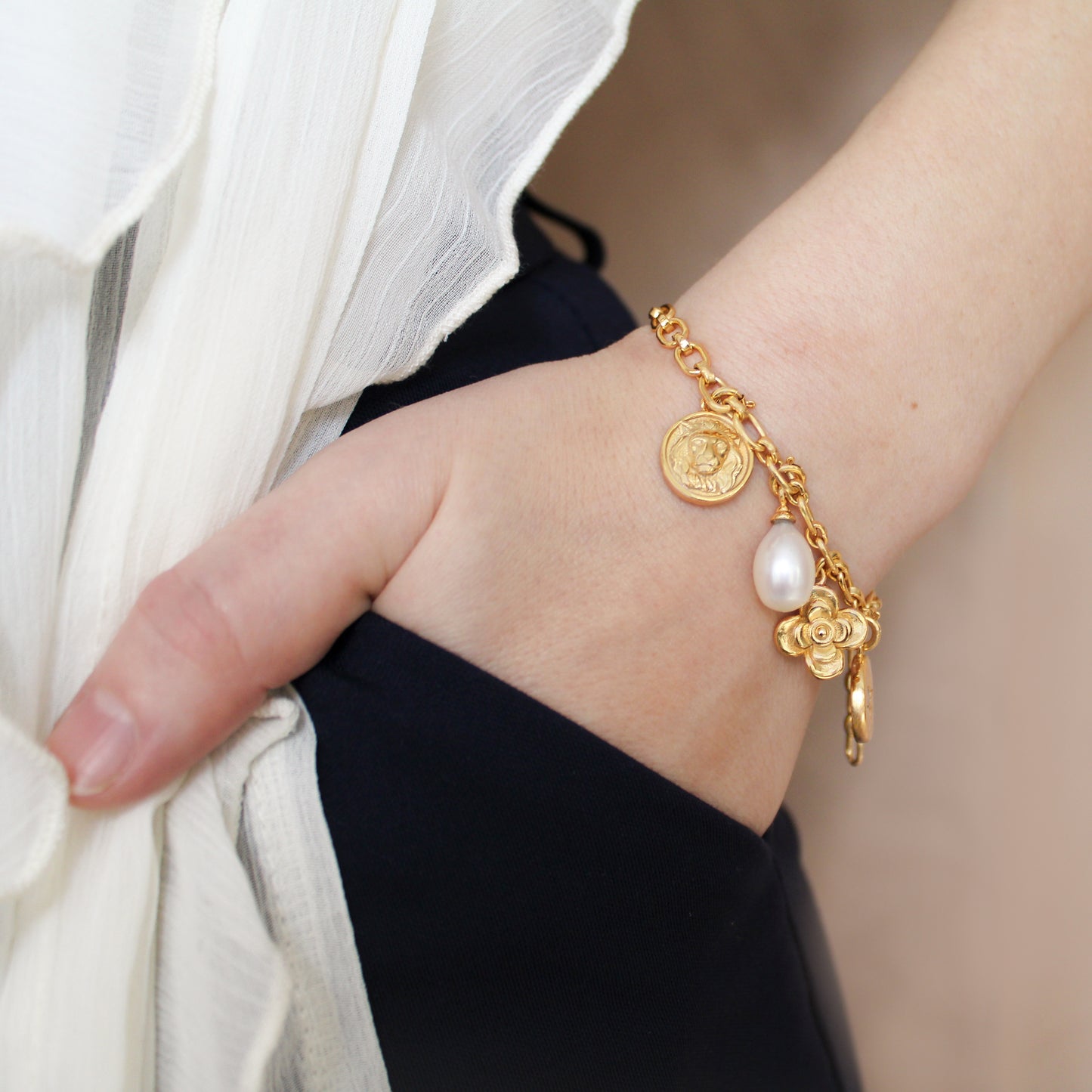 Gold archivist bracelet with charms on a wrist against a neutral background