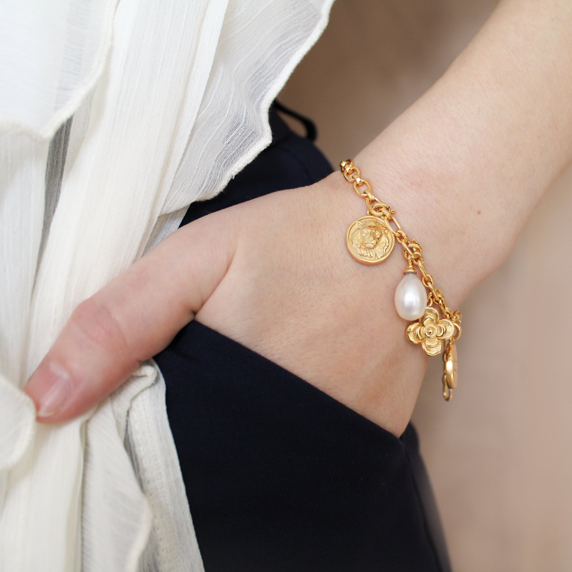Gold archivist bracelet with charms on a wrist against a neutral background