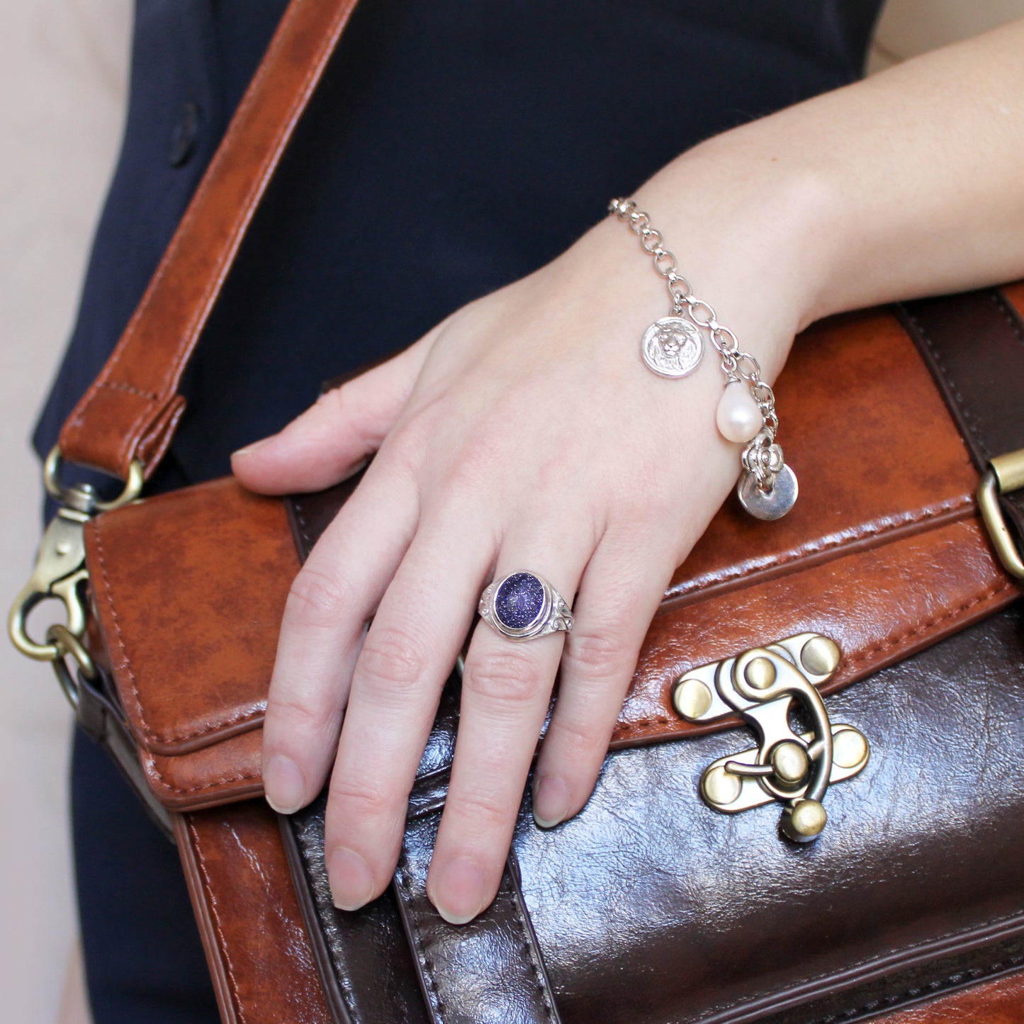 Hand with ring and charm bracelet holding a brown leather handbag