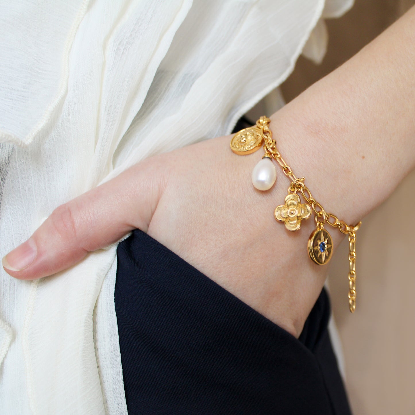 Gold archivist bracelet with charms on a wrist against a neutral background