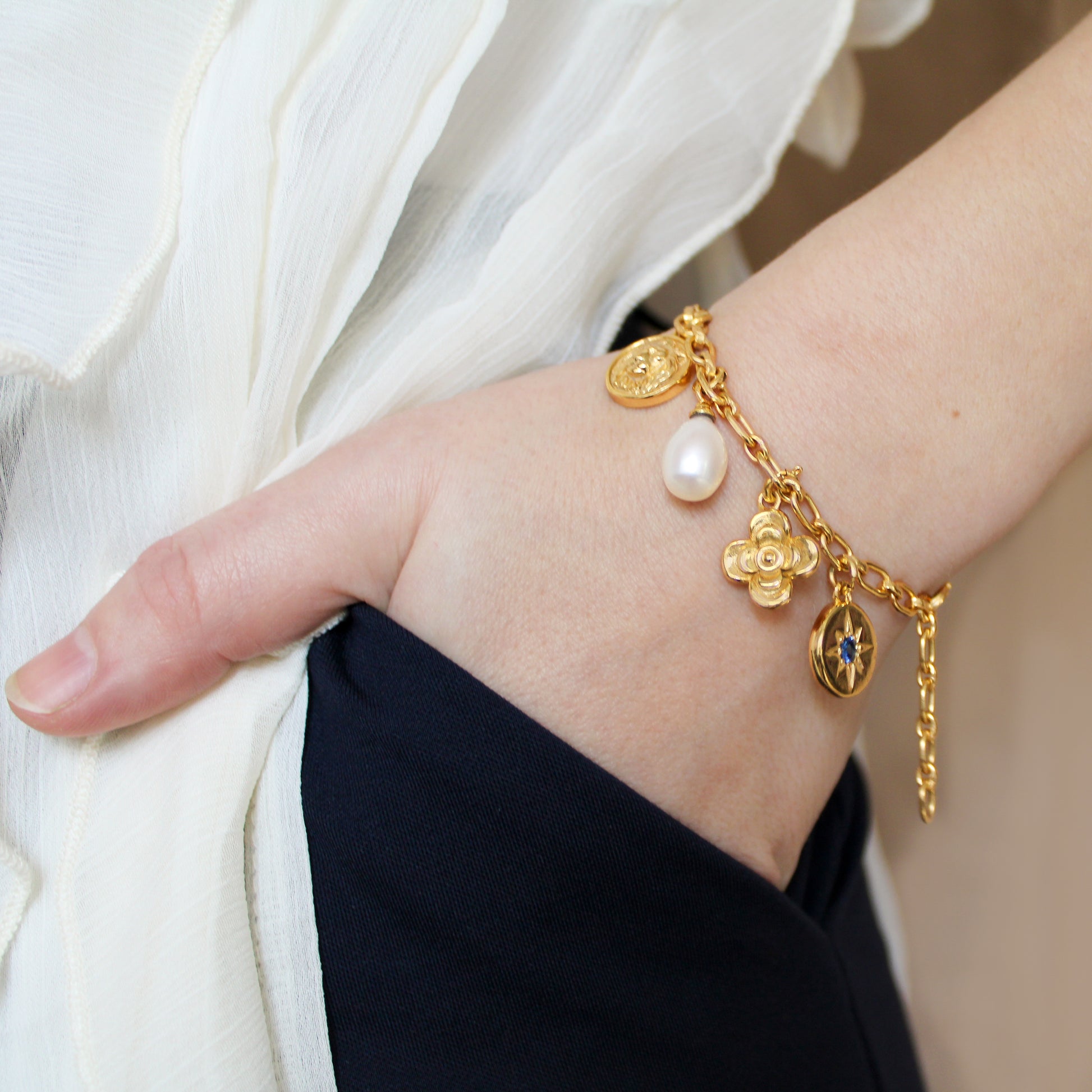 Gold archivist bracelet with charms on a wrist against a neutral background