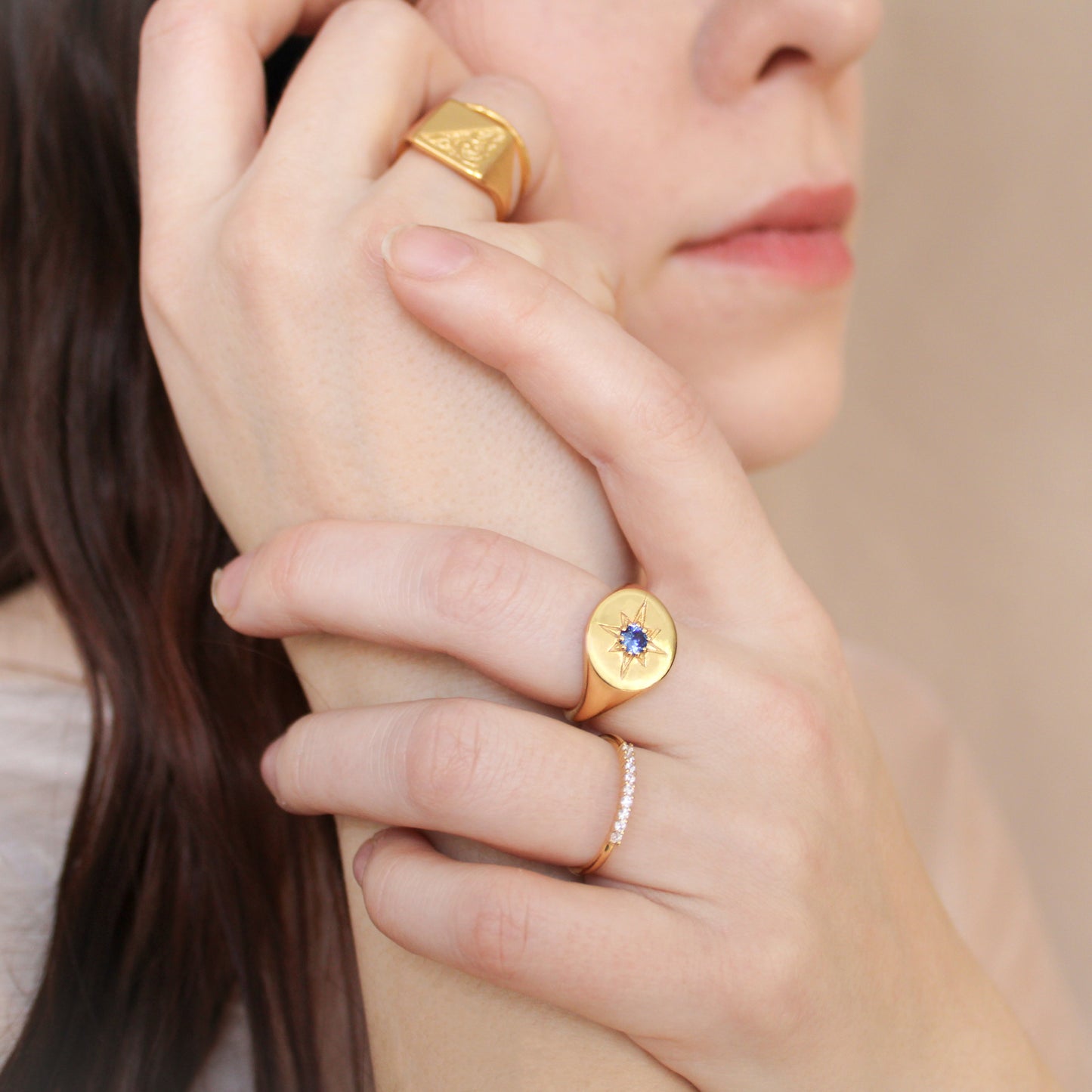 Close-up of a person wearing two gold signet rings with gemstones on a neutral background