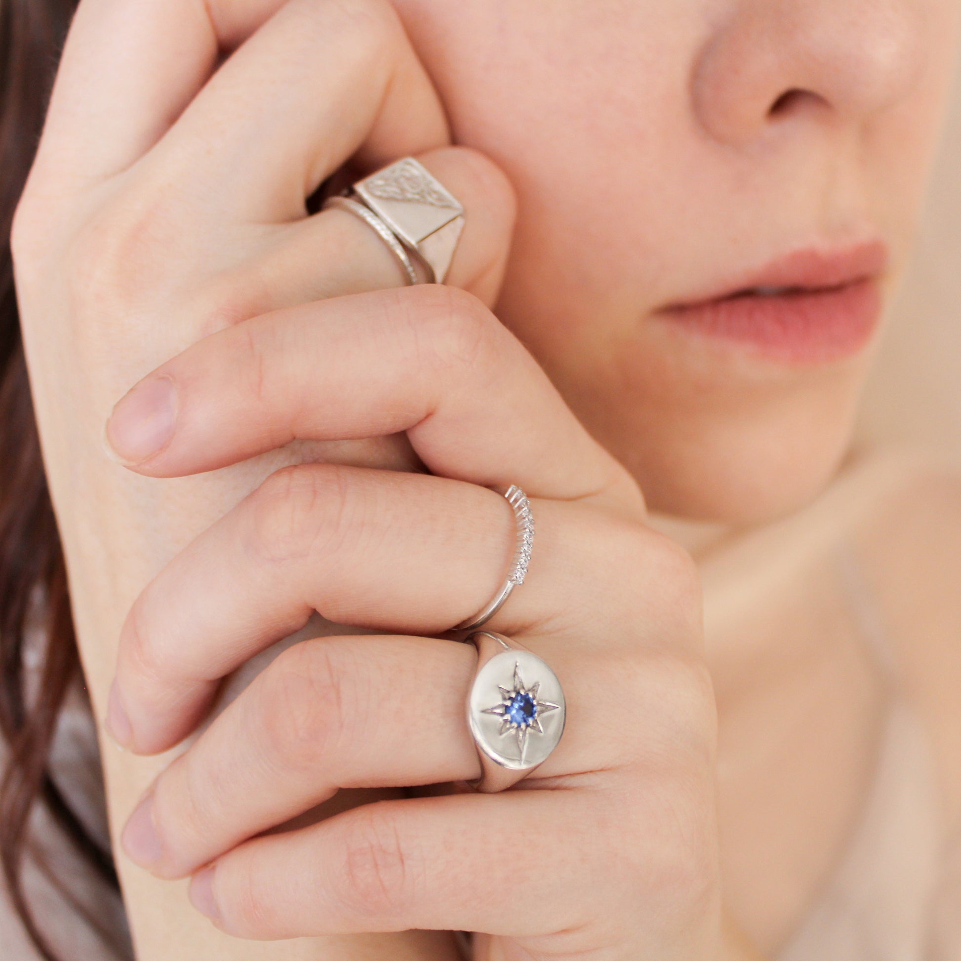 Close-up of a hand wearing Wayfinder and architect signet rings with a focus on one ring with a blue gemstone.