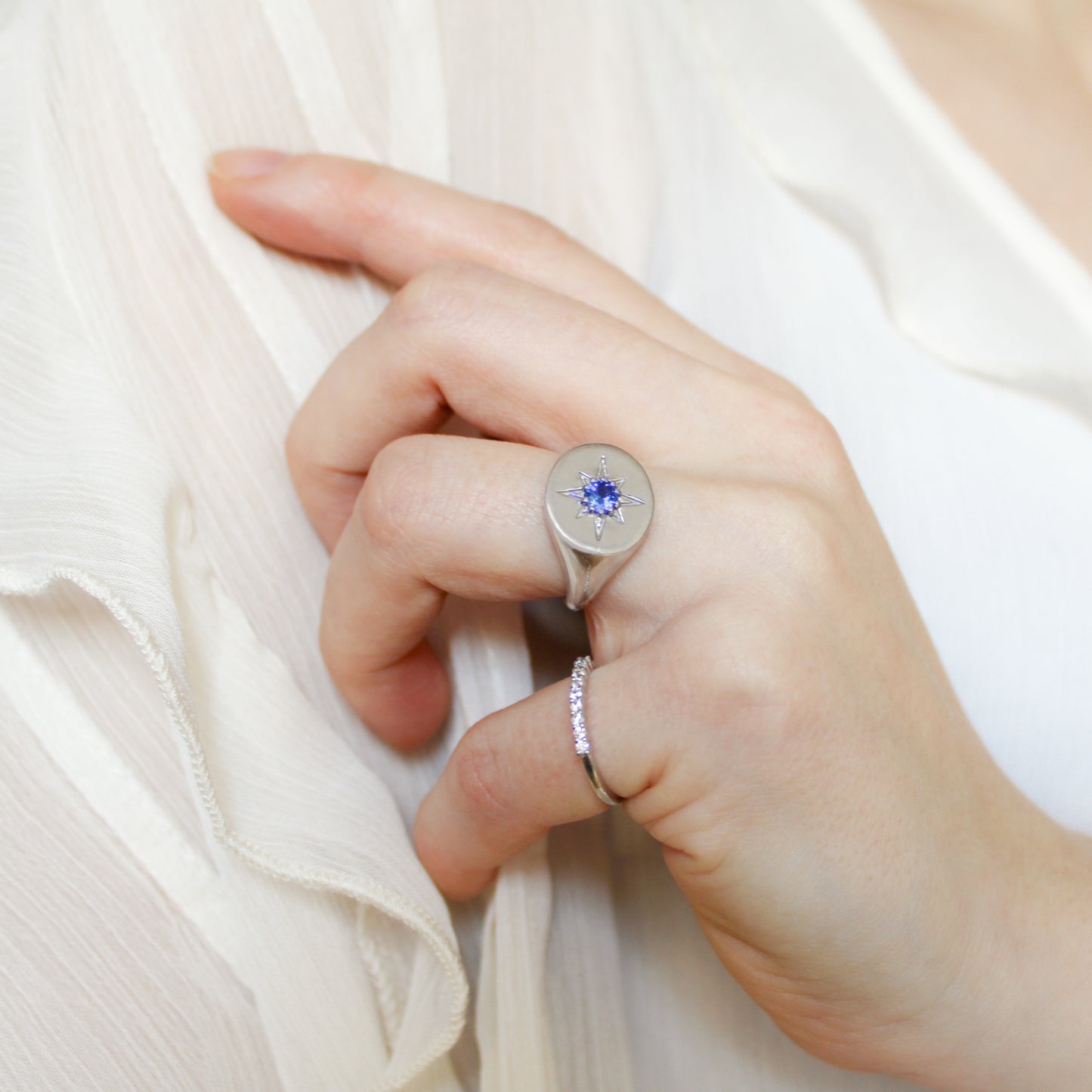 Close-up of a hand wearing Wayfinder signet ring and stacker ring on a light background
