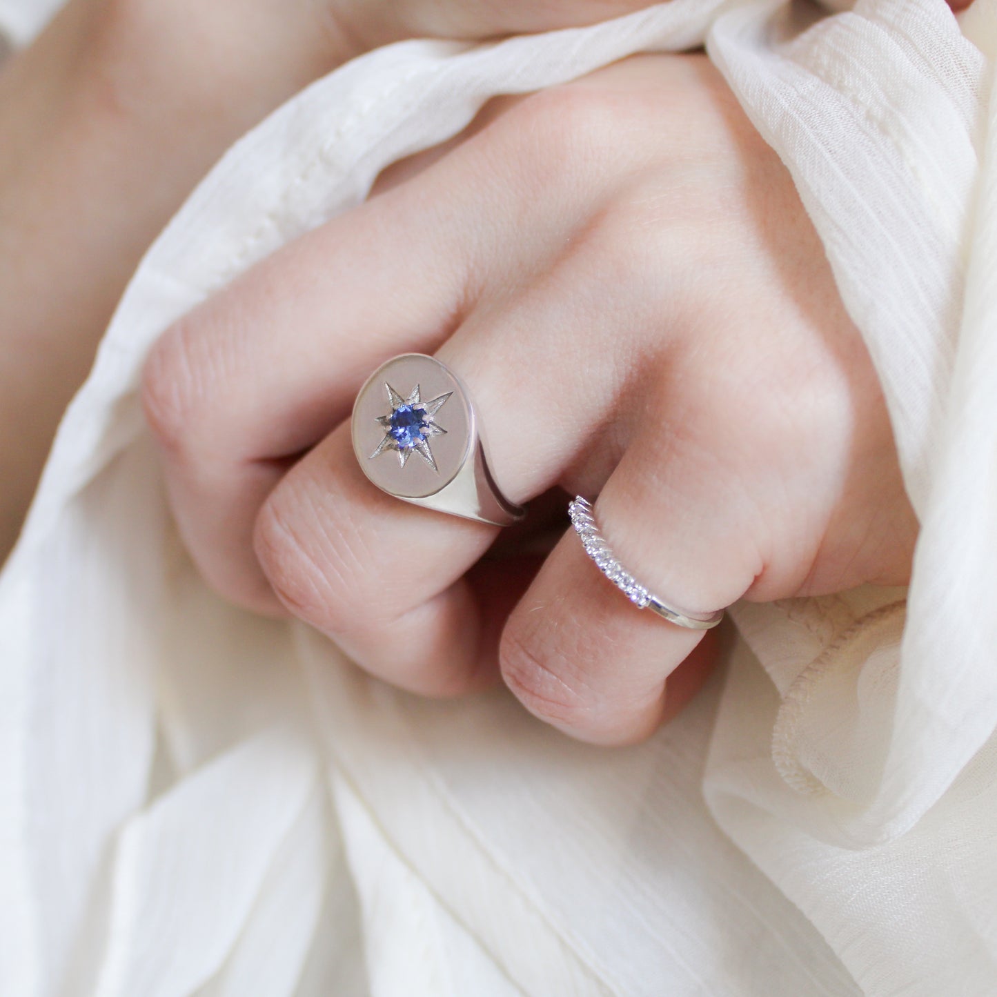 Close-up of a hand wearing two silver signet rings with gemstones and star engraving on a white fabric background