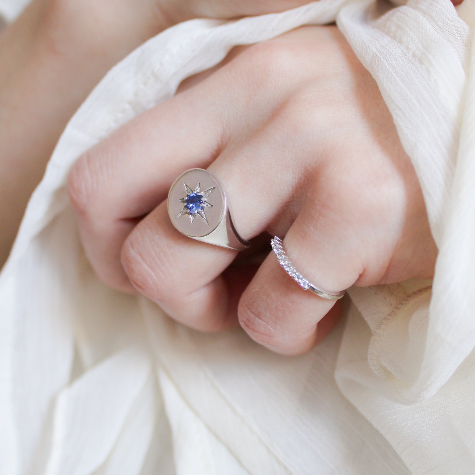 Close-up of a hand wearing two silver signet rings with gemstones and star engraving on a white fabric background