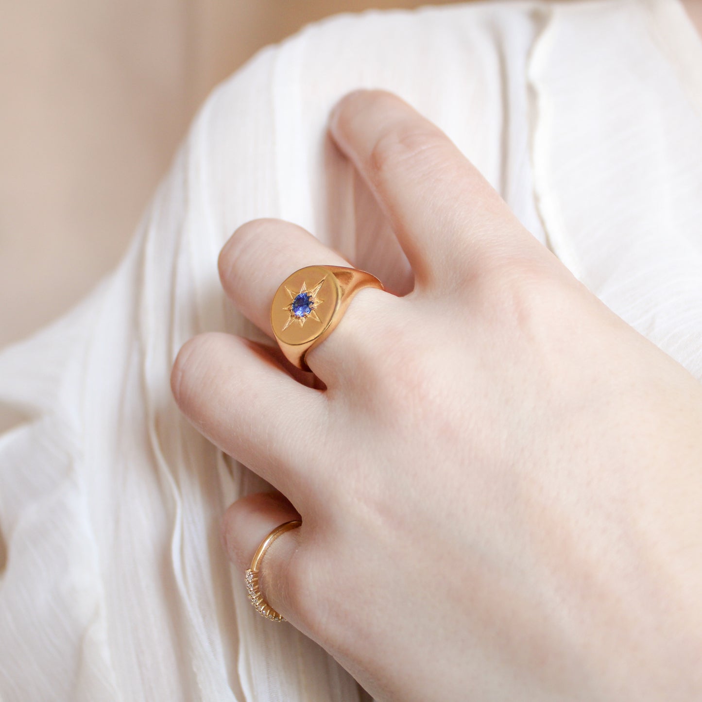 Gold Wayfinder signet ring with a blue gemstone and star engraving on a hand against a white fabric background